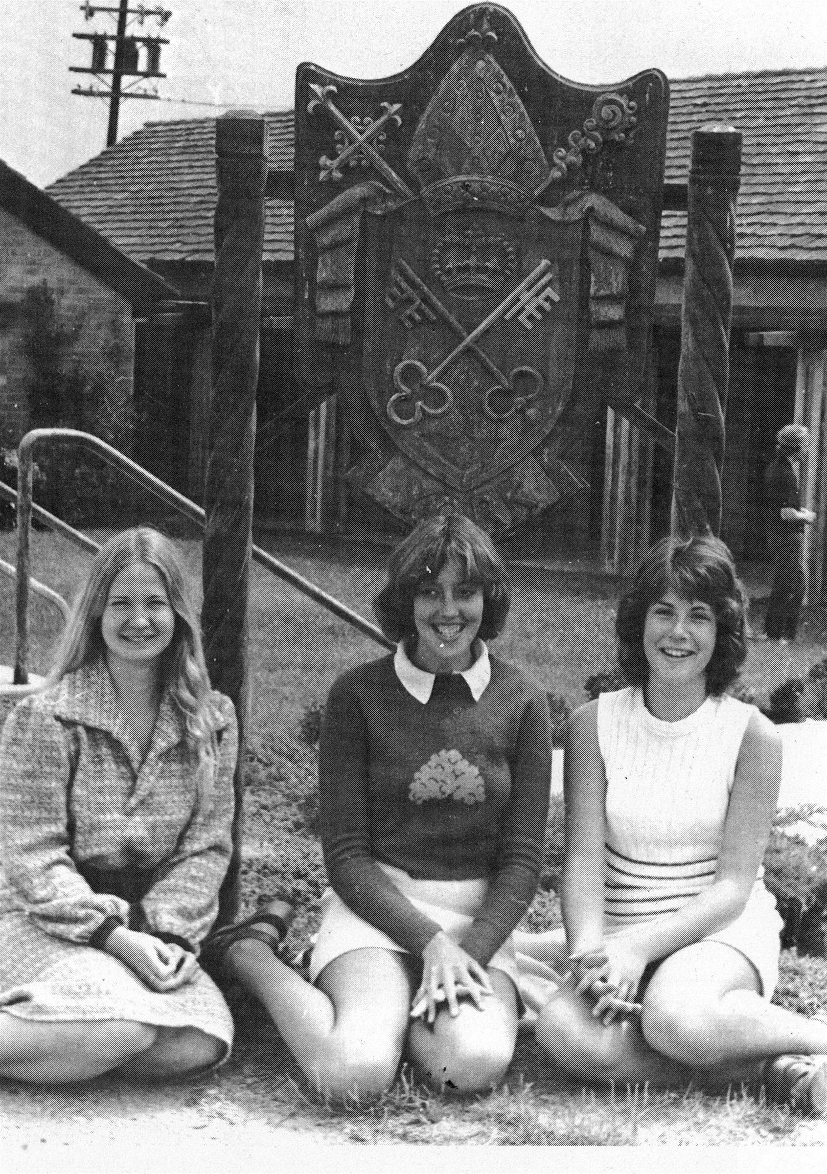 black and white photo of 3 girls in front of school sign